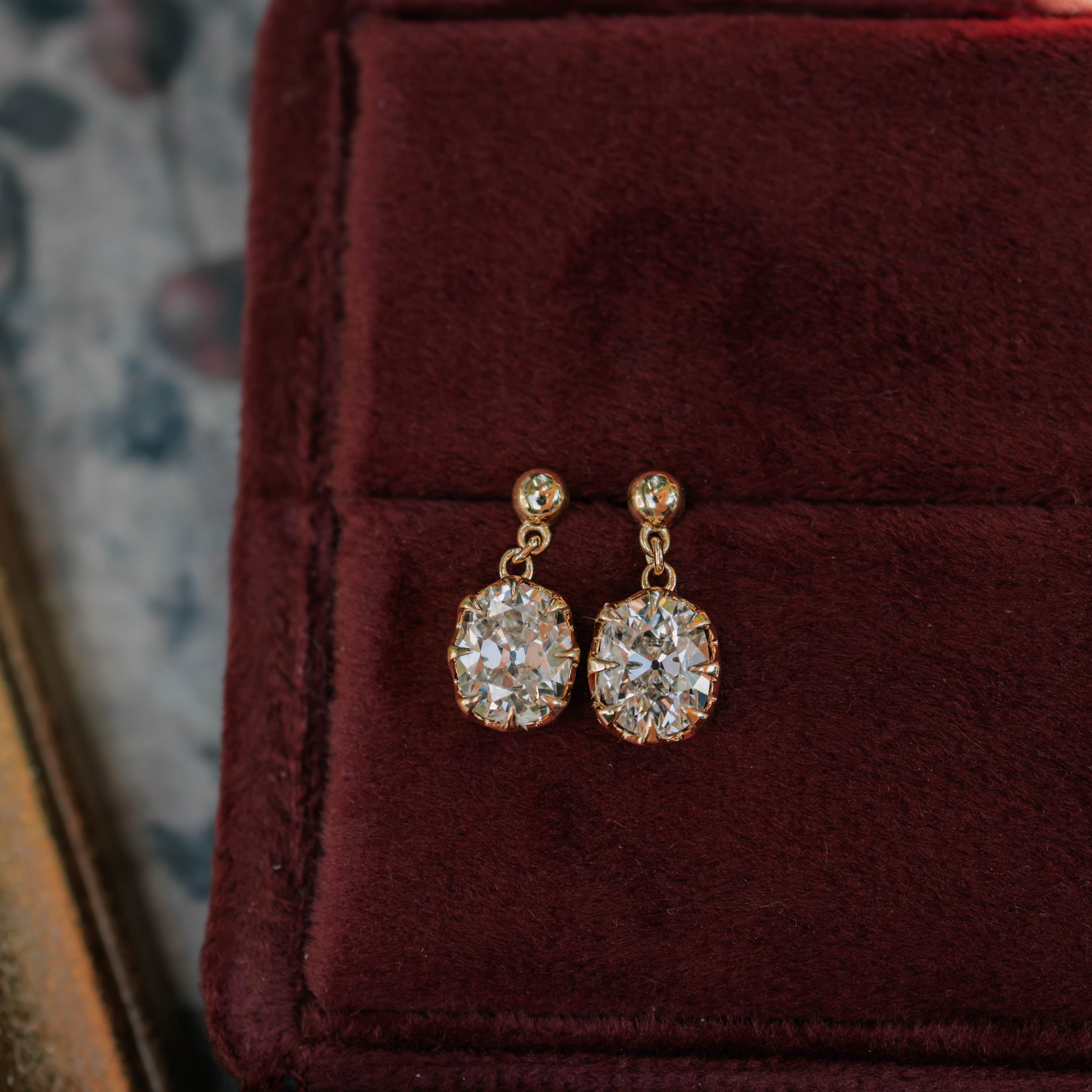 A pair of gold dangle earrings with clear rectangular gemstones resting in an open burgundy velvet jewelry box.