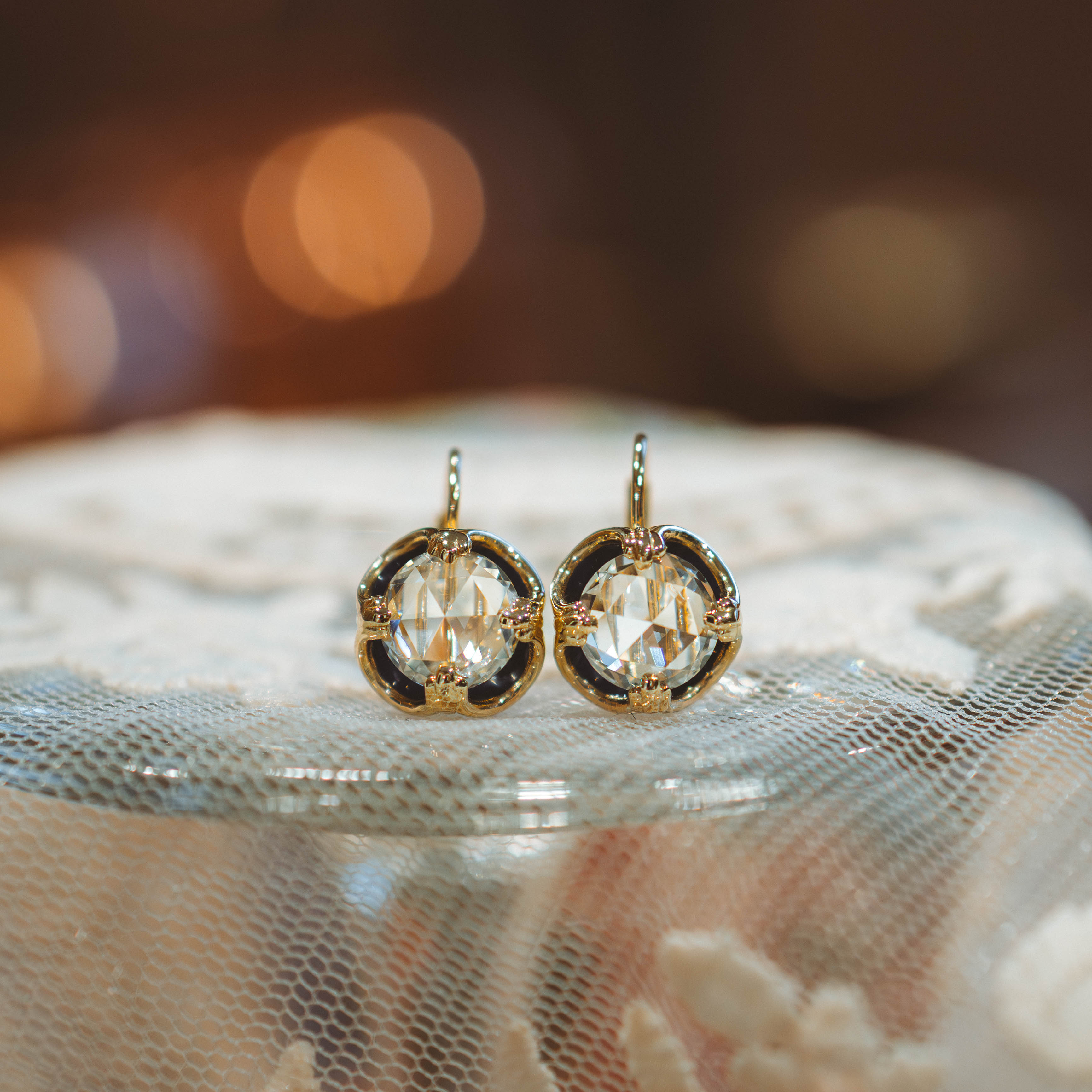 Gold, enamel,
and diamond rose cut earrings on a textured surface with a blurred background.