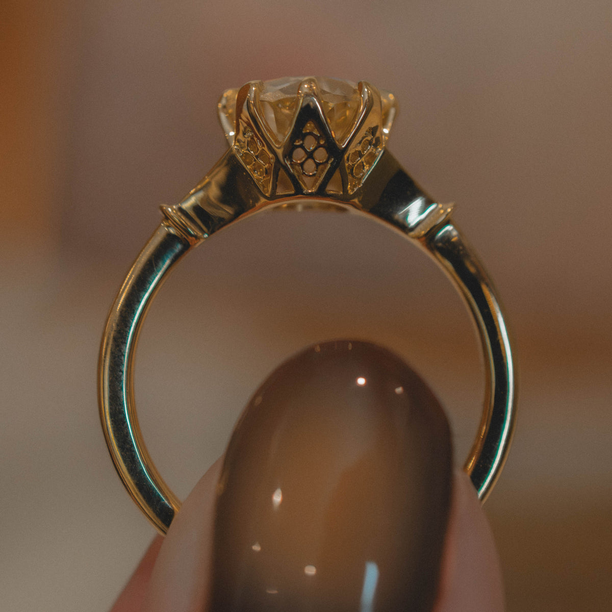 A close-up of a gold ring held between fingers, showing gothic arch basket profile