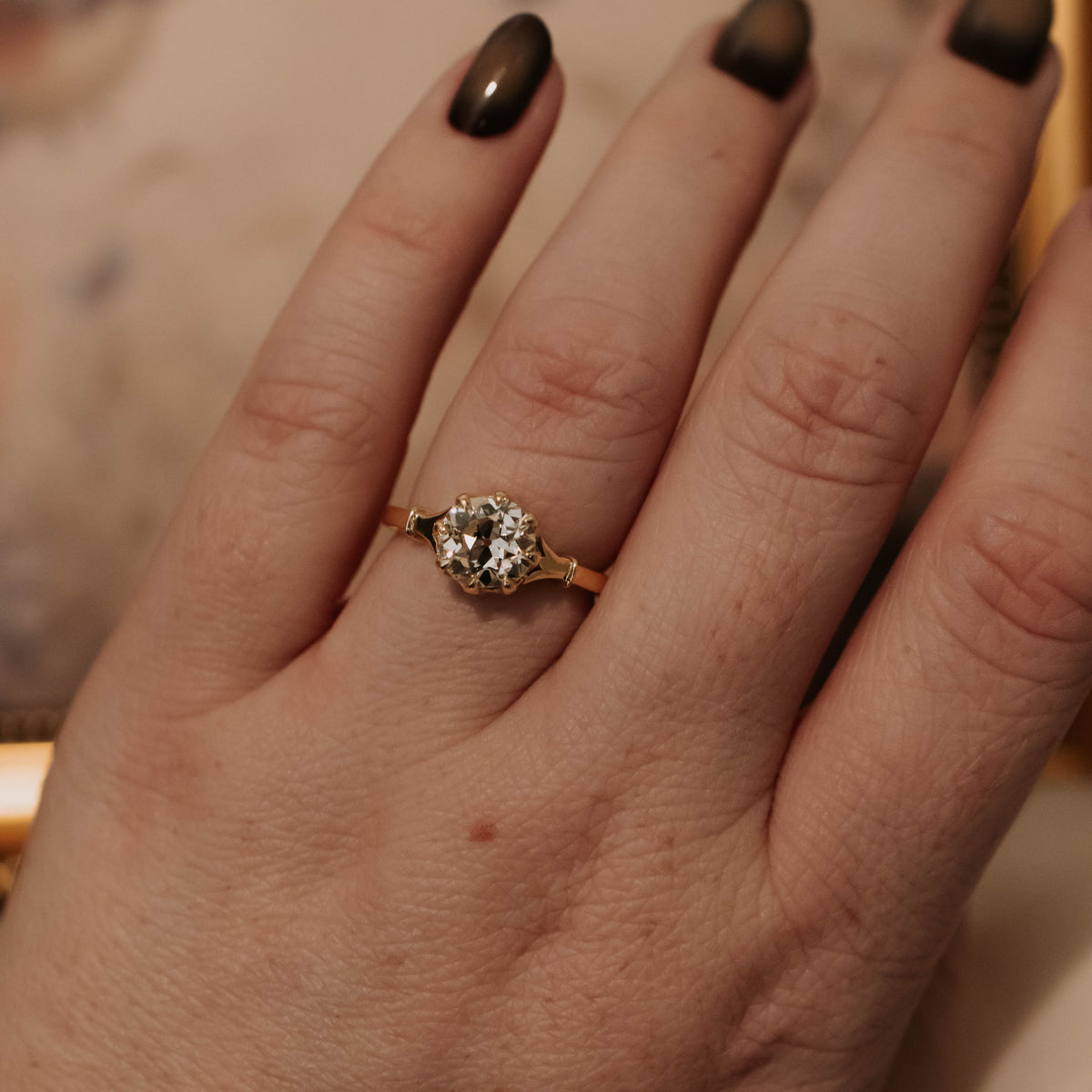 A close-up of a hand wearing a vintage-style gold ring with a round old mine diamond in yellow gold