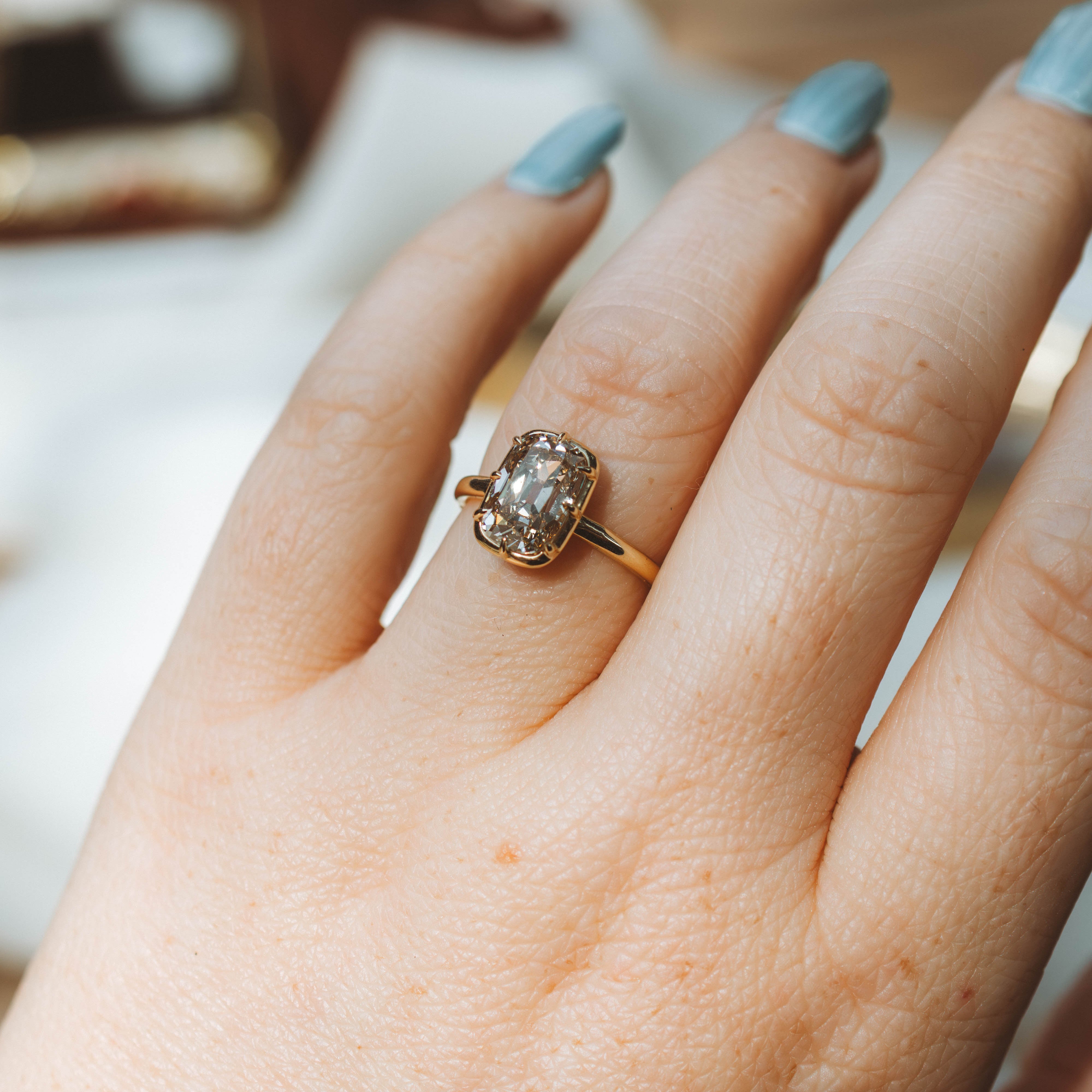 Hand wearing a champagne diamond ring with a blurred background