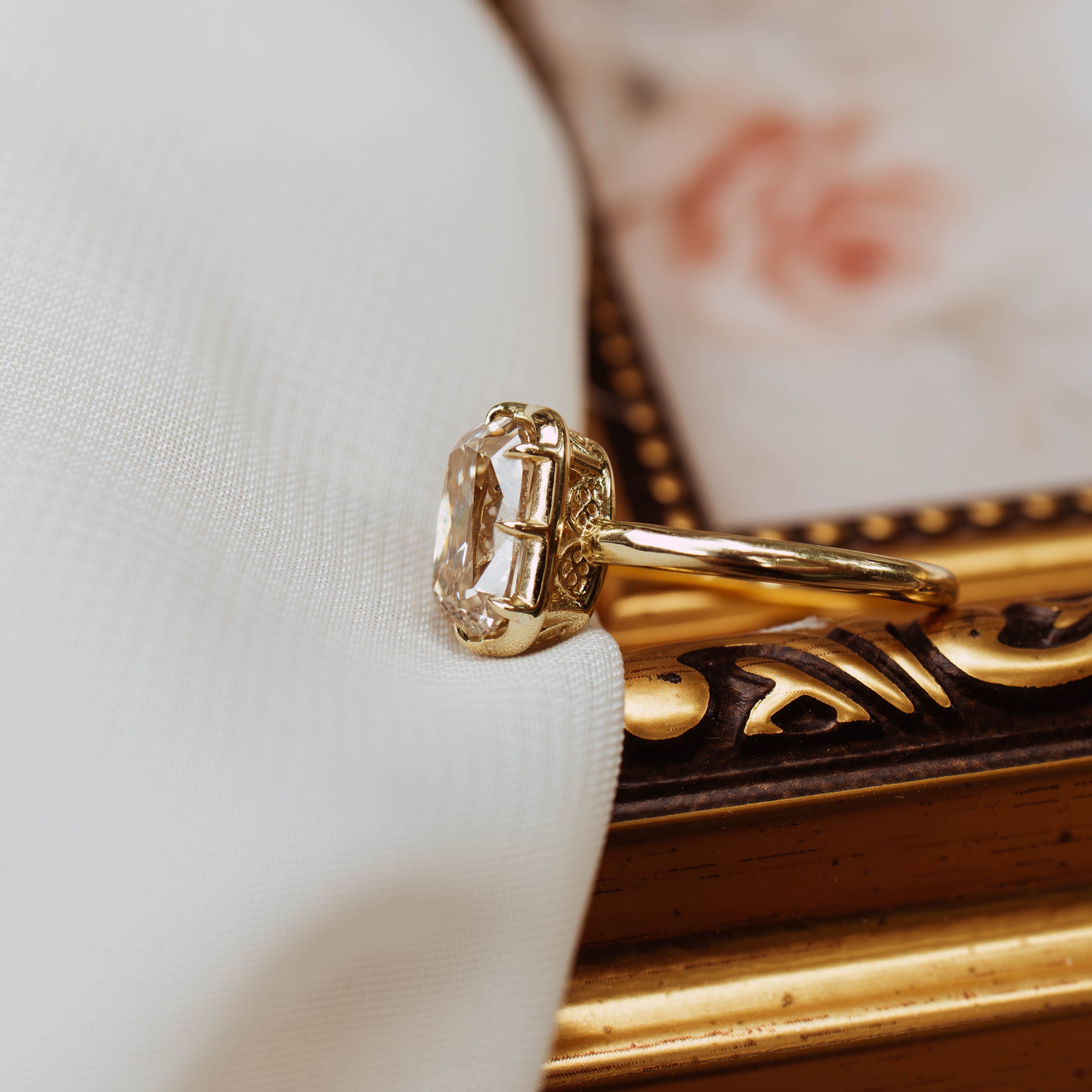 Gold ring with a diamond on a white cushion next to an ornate gold box.