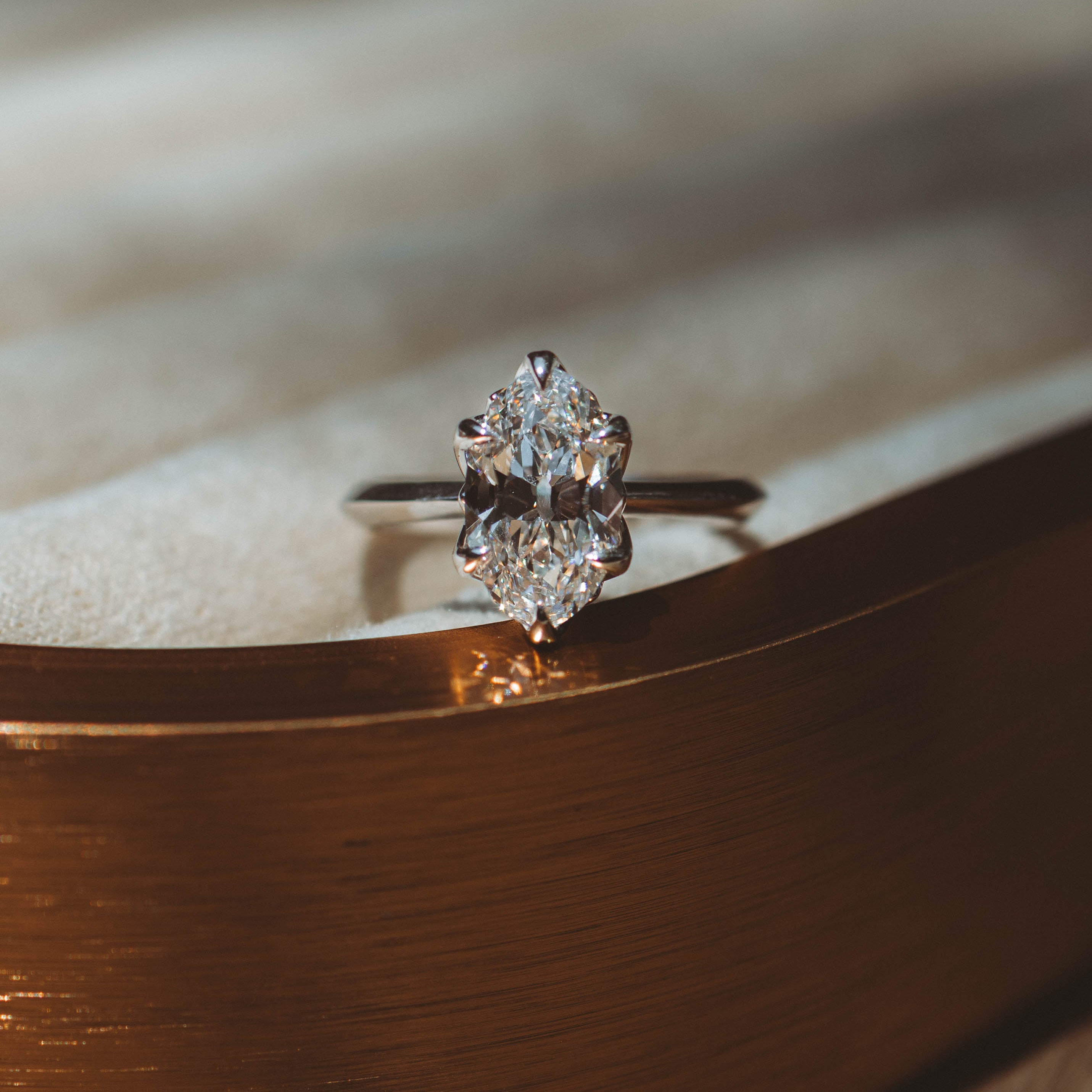 white gold moval diamond engagement ring on bronze textured surface with blurred background