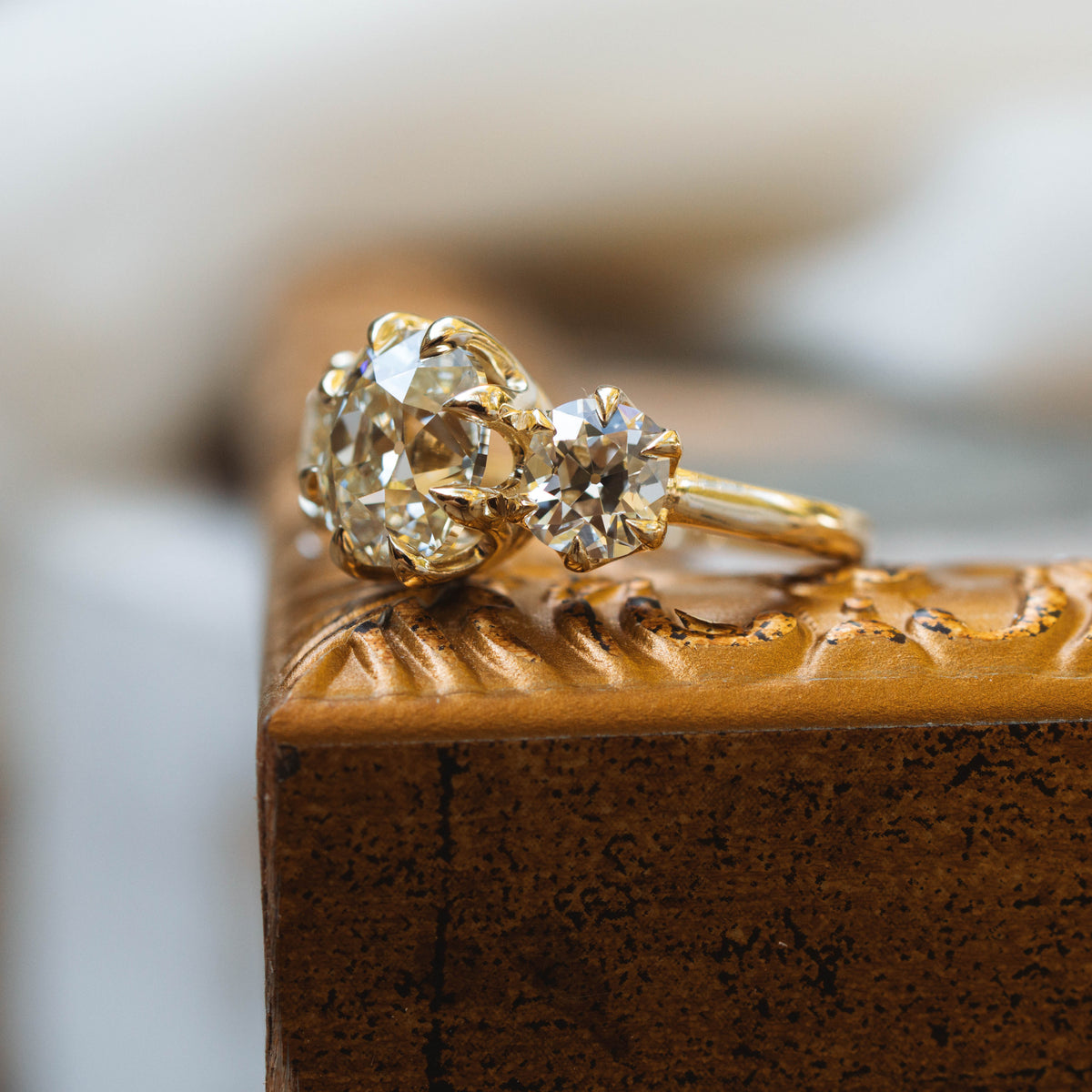 three stone old mine cut diamond ring in yellow gold sitting on gold frame.