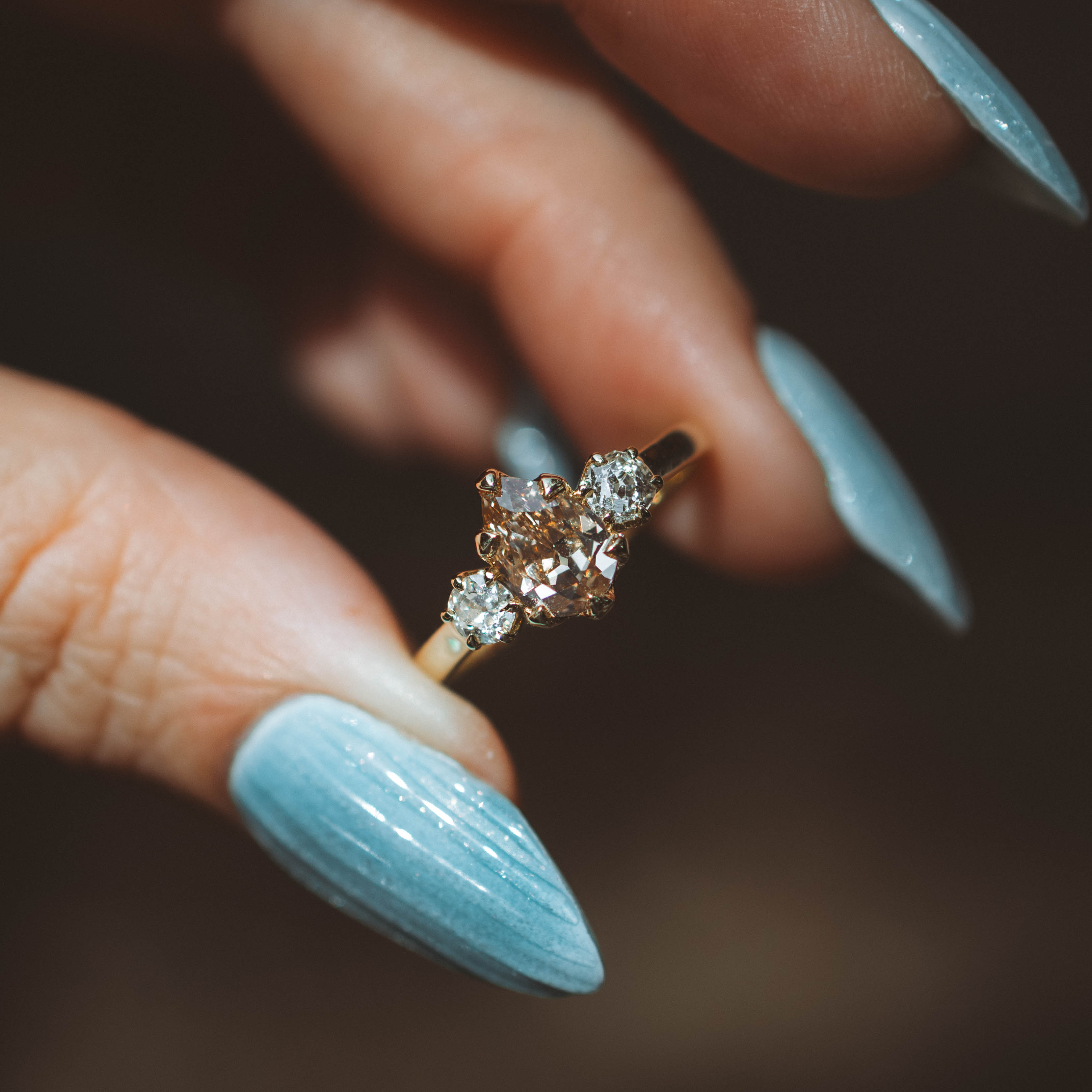 Close-up of a hand holding a 3 stone diamond ring with a blurred background