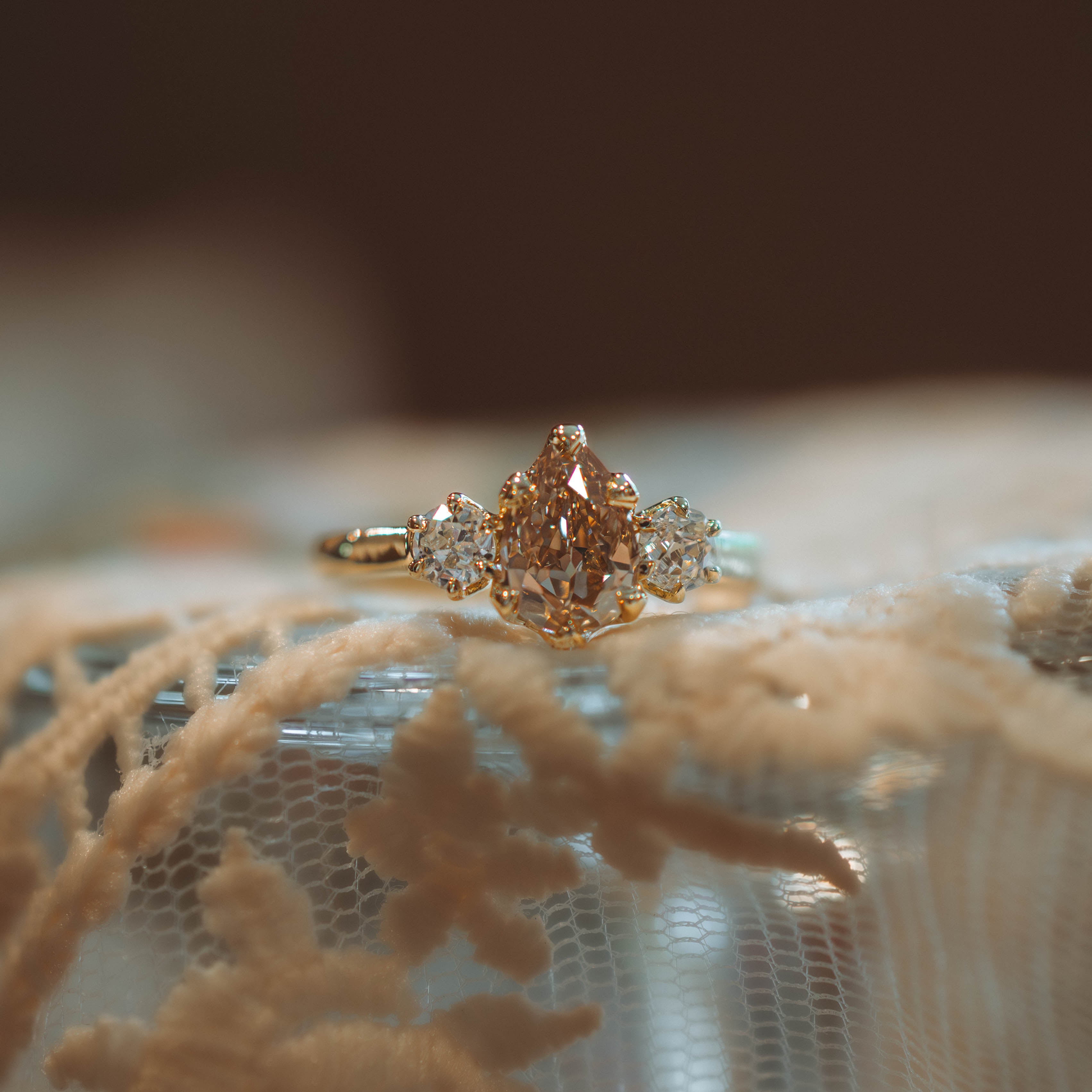 Gold ring with a large diamond and smaller stones on a textured lace surface