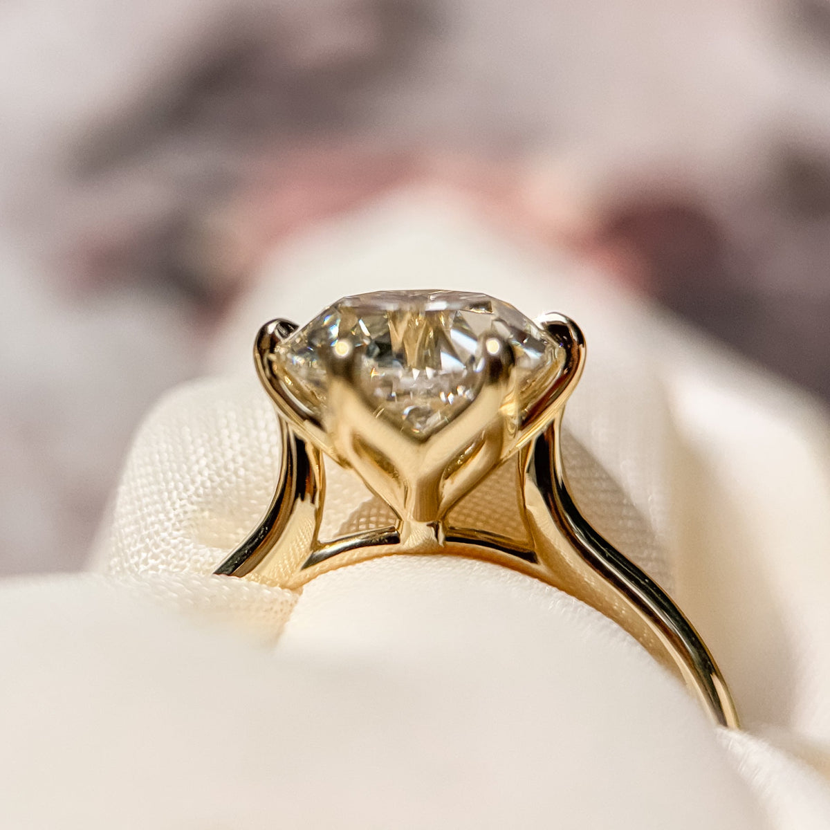 A close-up shot of a yellow gold solitaire ring with a round old european diamond resting on a white satin surface with a soft, blurred background.
