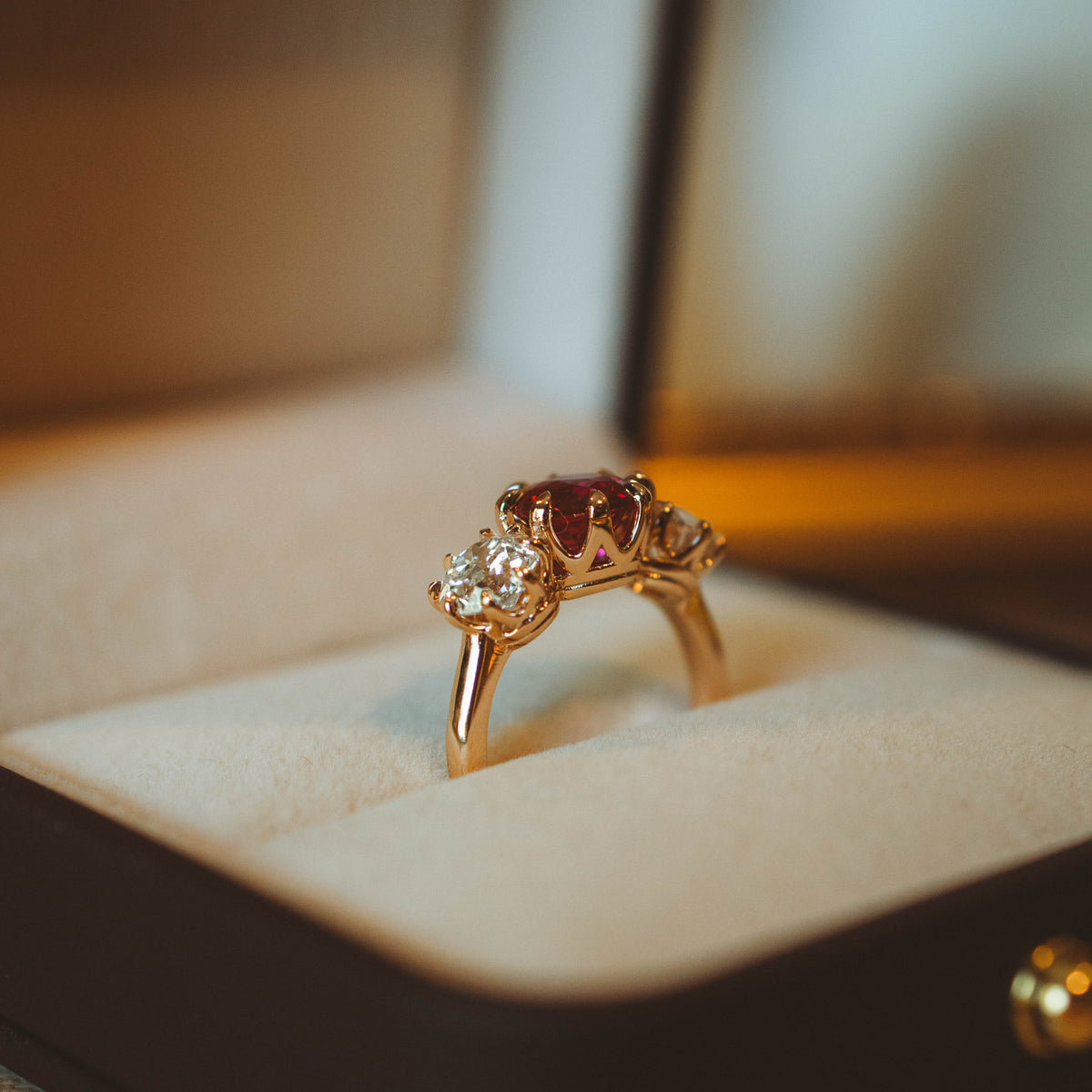 profile basket view of ruby and diamond trilogy engagement ring. show standng upright in right box. set in rose gold.