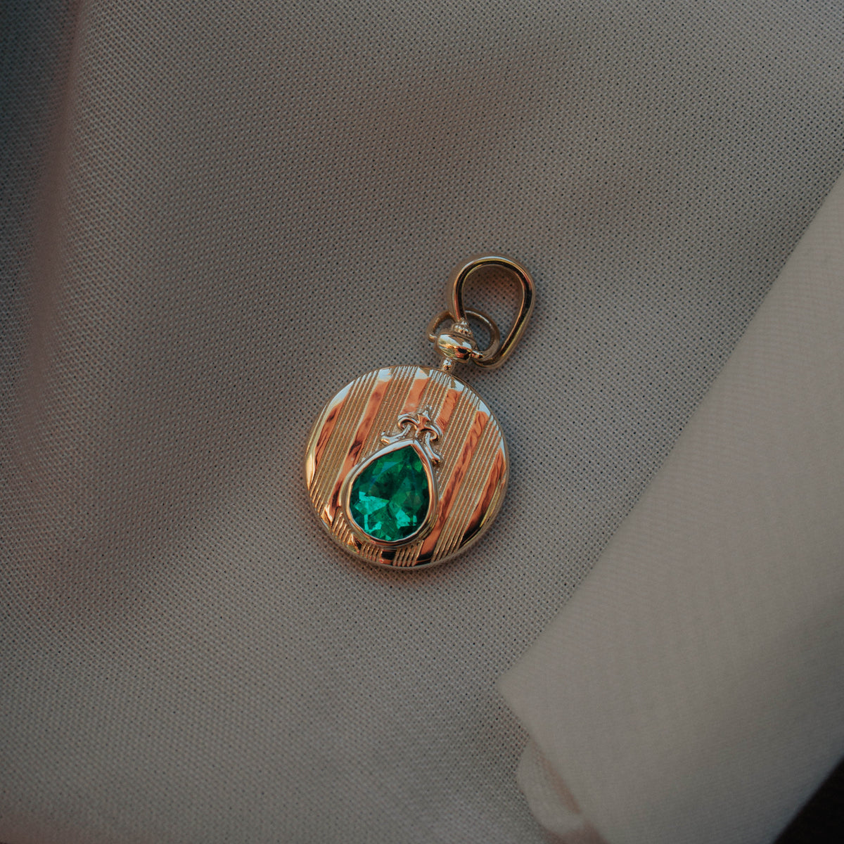14k yellow gold coin pendant on white background featured engraved strike detail and pear shaped emerald center gemstone