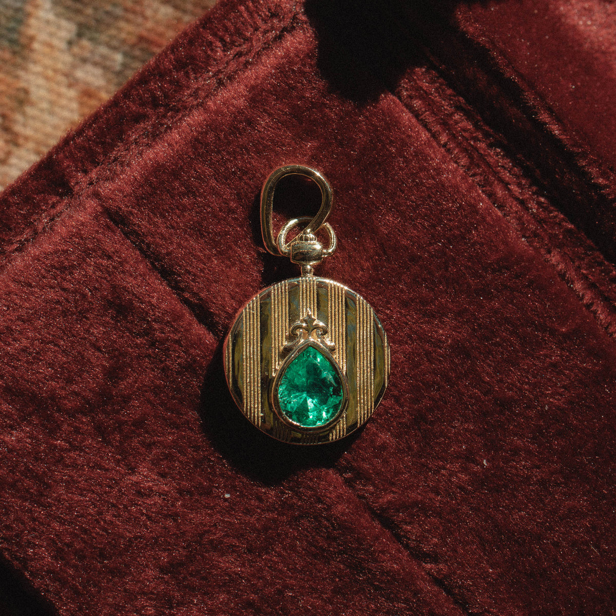 yellow gold coin pendant on red velvet background featured engraved strike detail and pear shaped emerald center gemstone