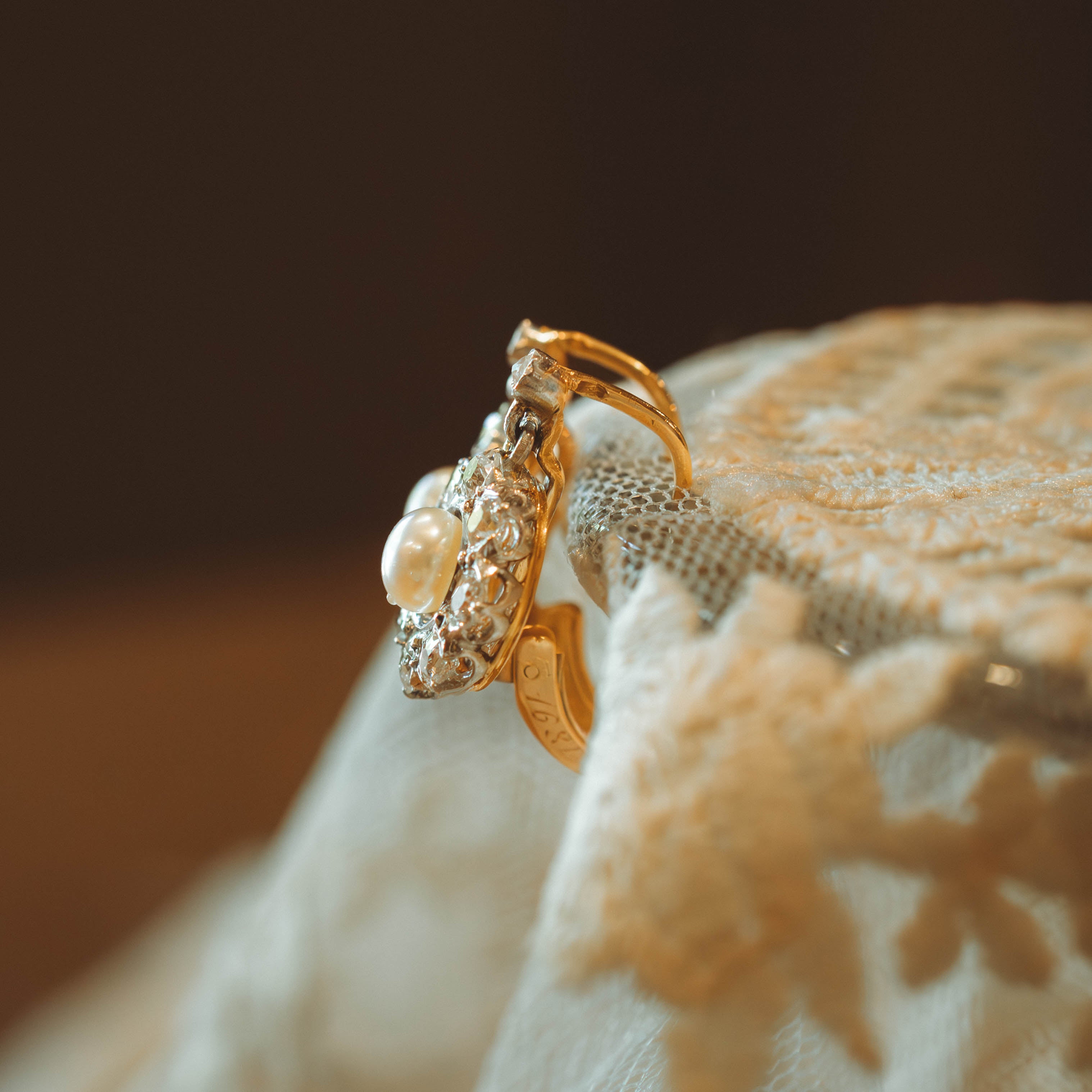 Gold earring with pearl and diamond on a lace textured surface