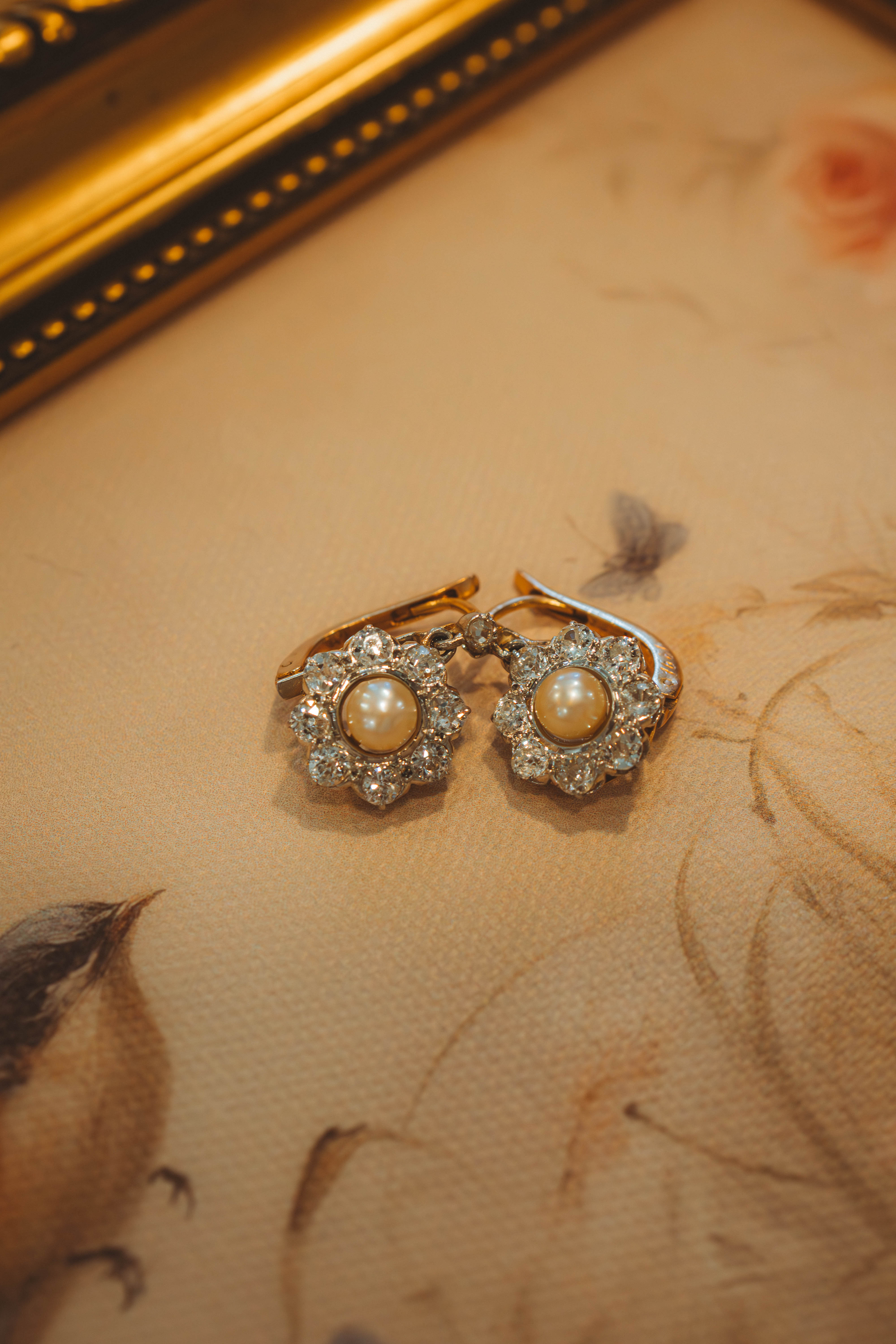 Pair of pearl and diamond earrings on a decorative surface with floral patterns