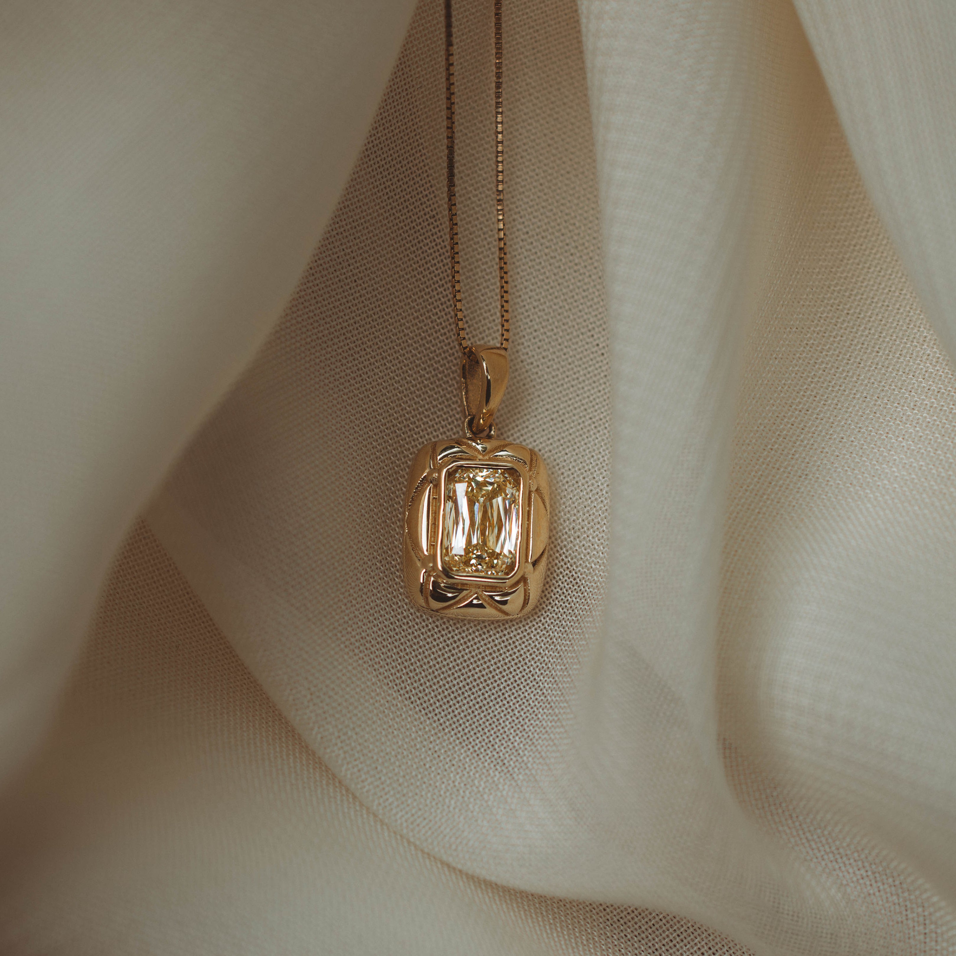 yellow gold pendant on chain on white fabric