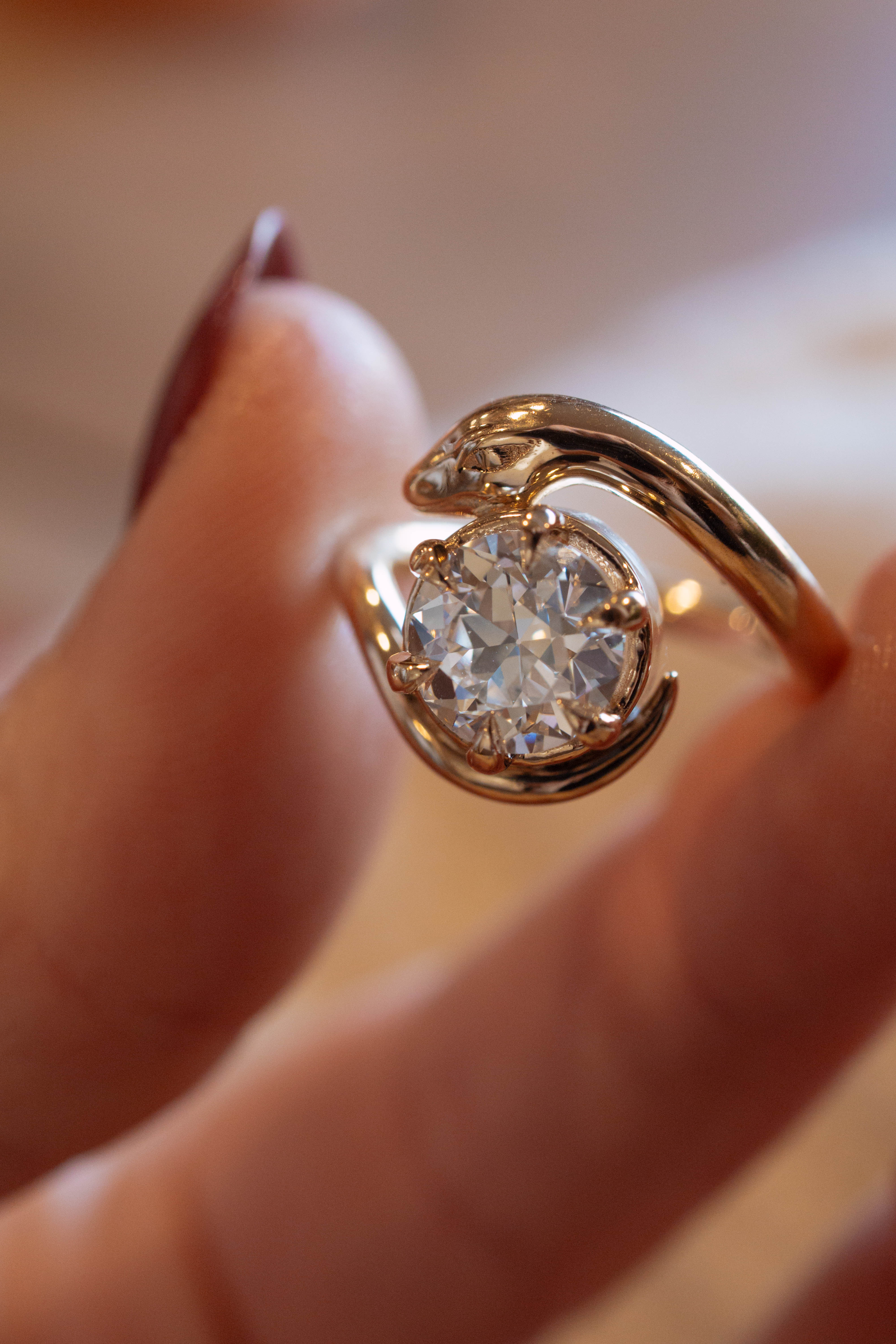 Gold diamond serpent ring with a diamond held between two fingers against a blurred background