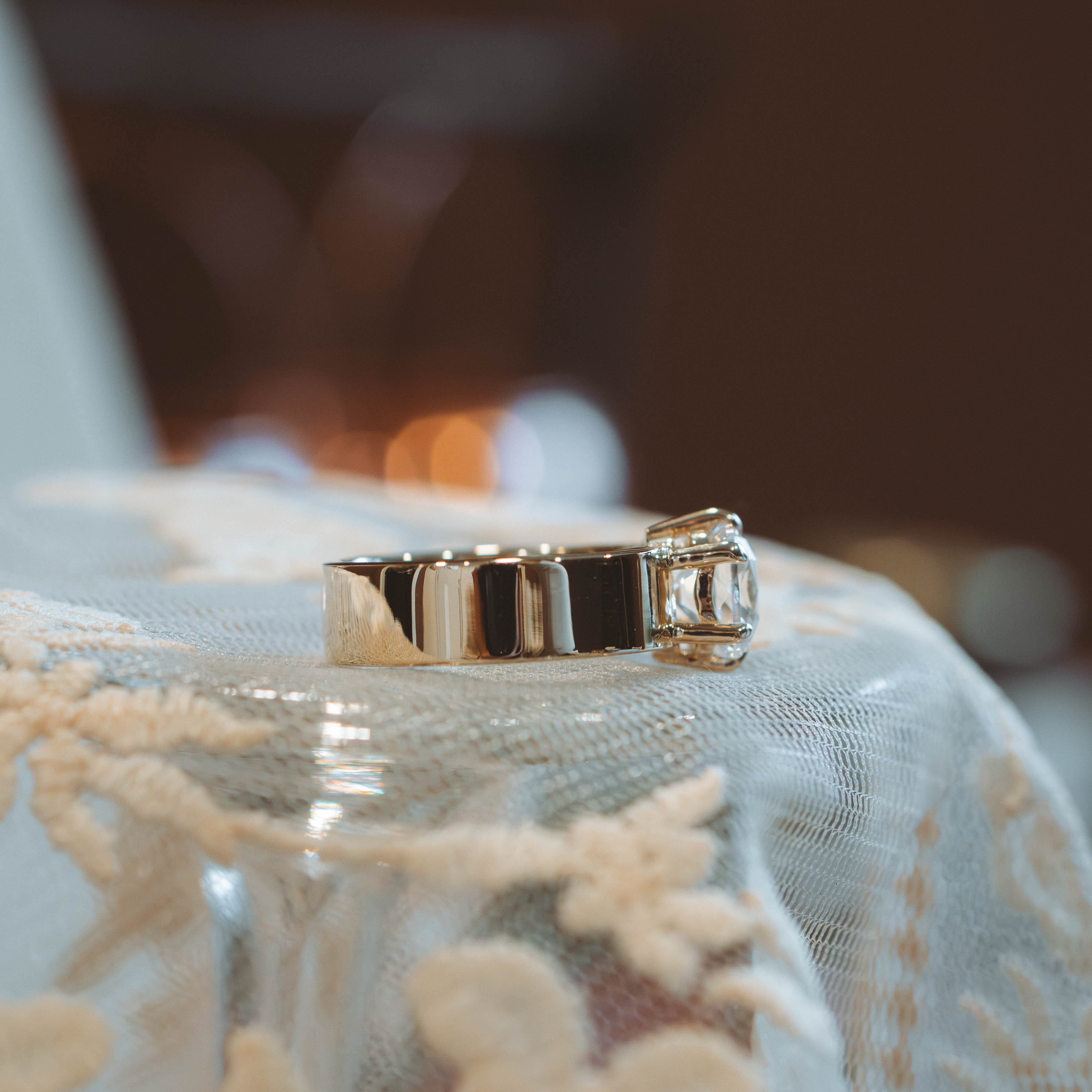 Gold diamond engagement ring on a textured surface with a blurred background