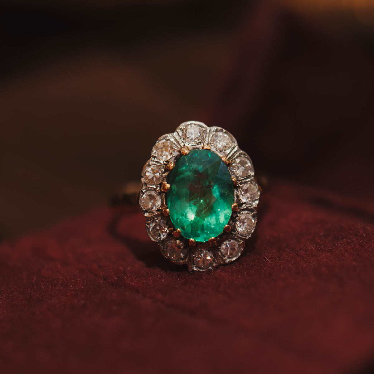 halo style ring with bright green center emerald surrounded by accent halo diamonds sitting on a red velvet jewel box. 