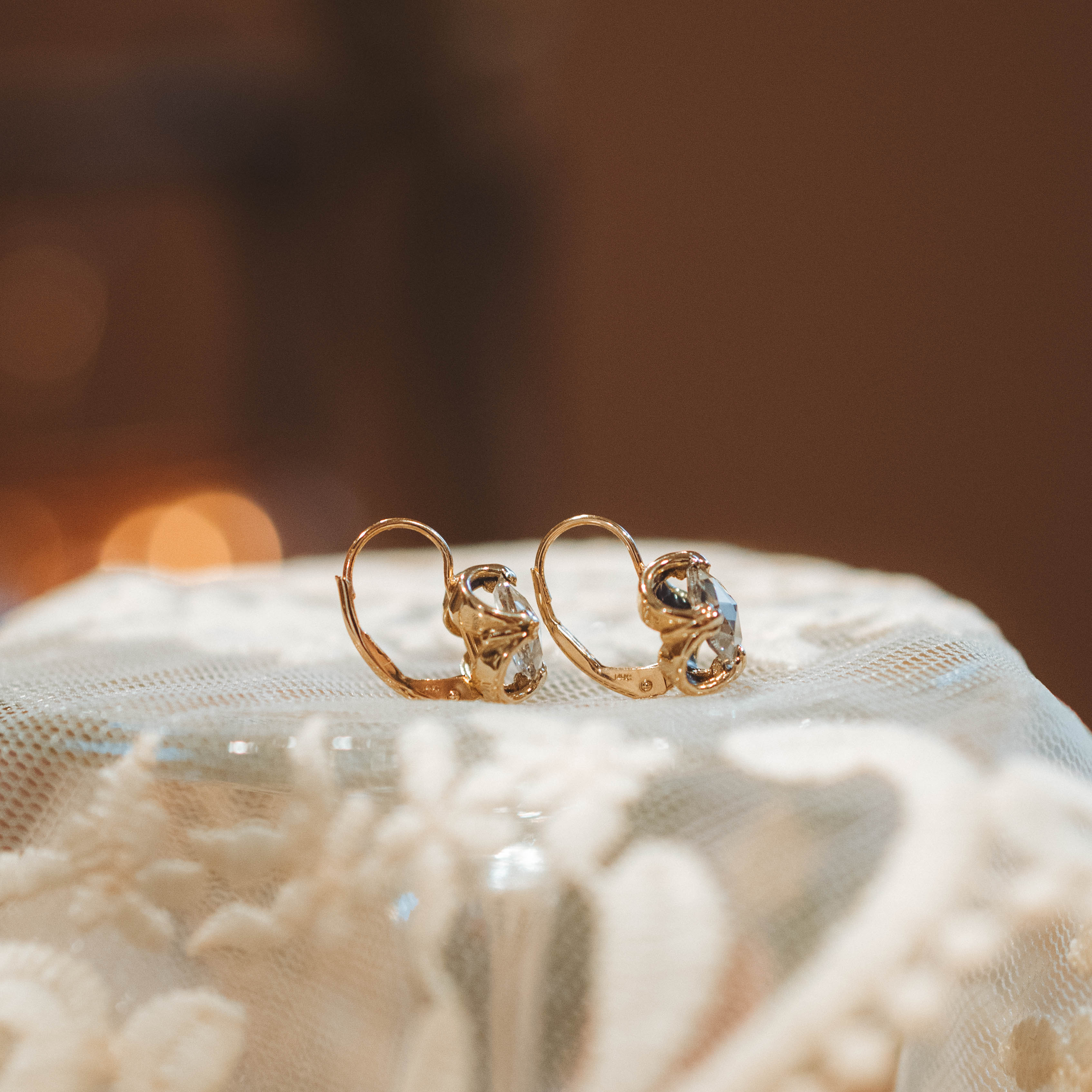 Gold earrings with diamonds on a textured surface with a blurred background