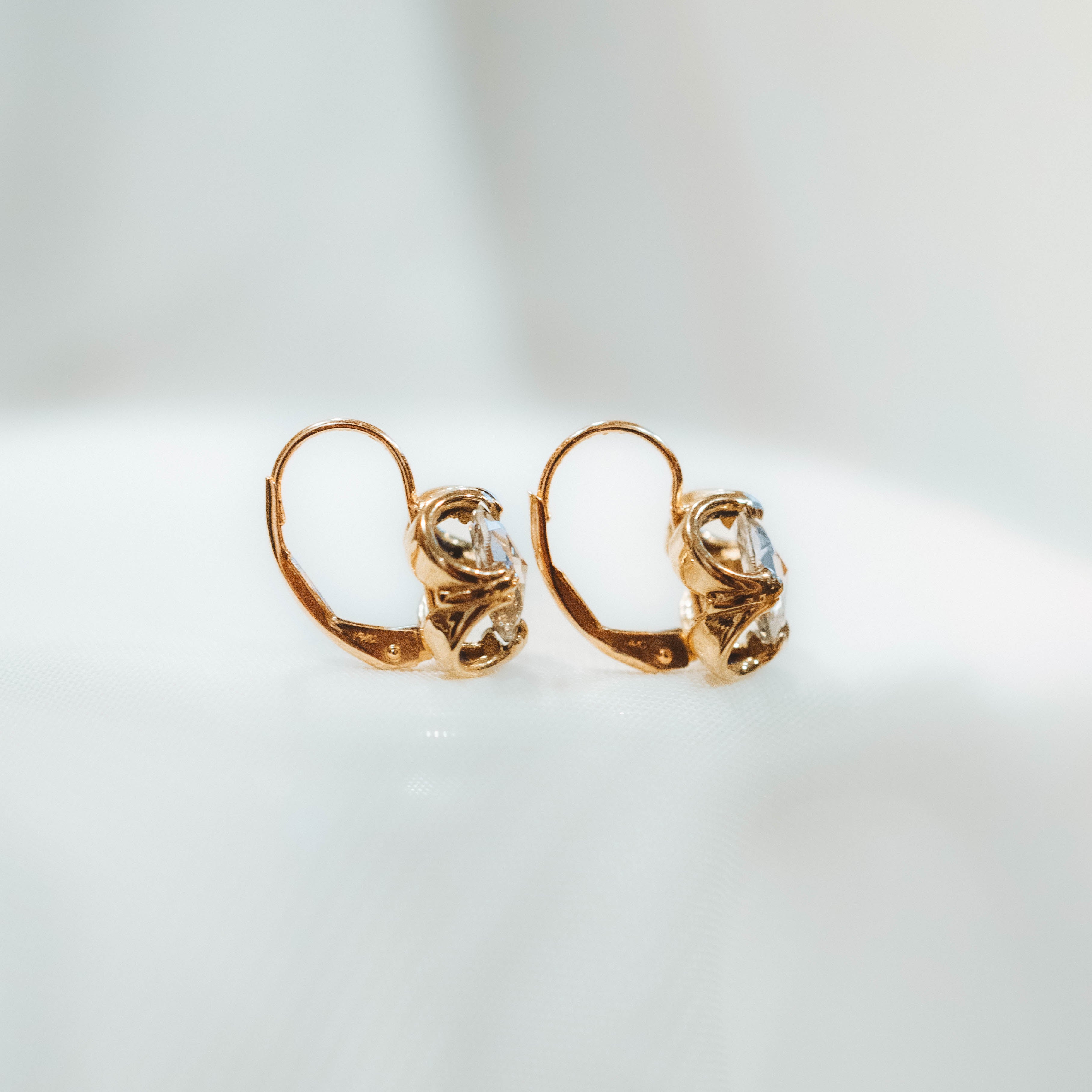 Pair of gold drop earrings with clear rose diamond on a light gray background