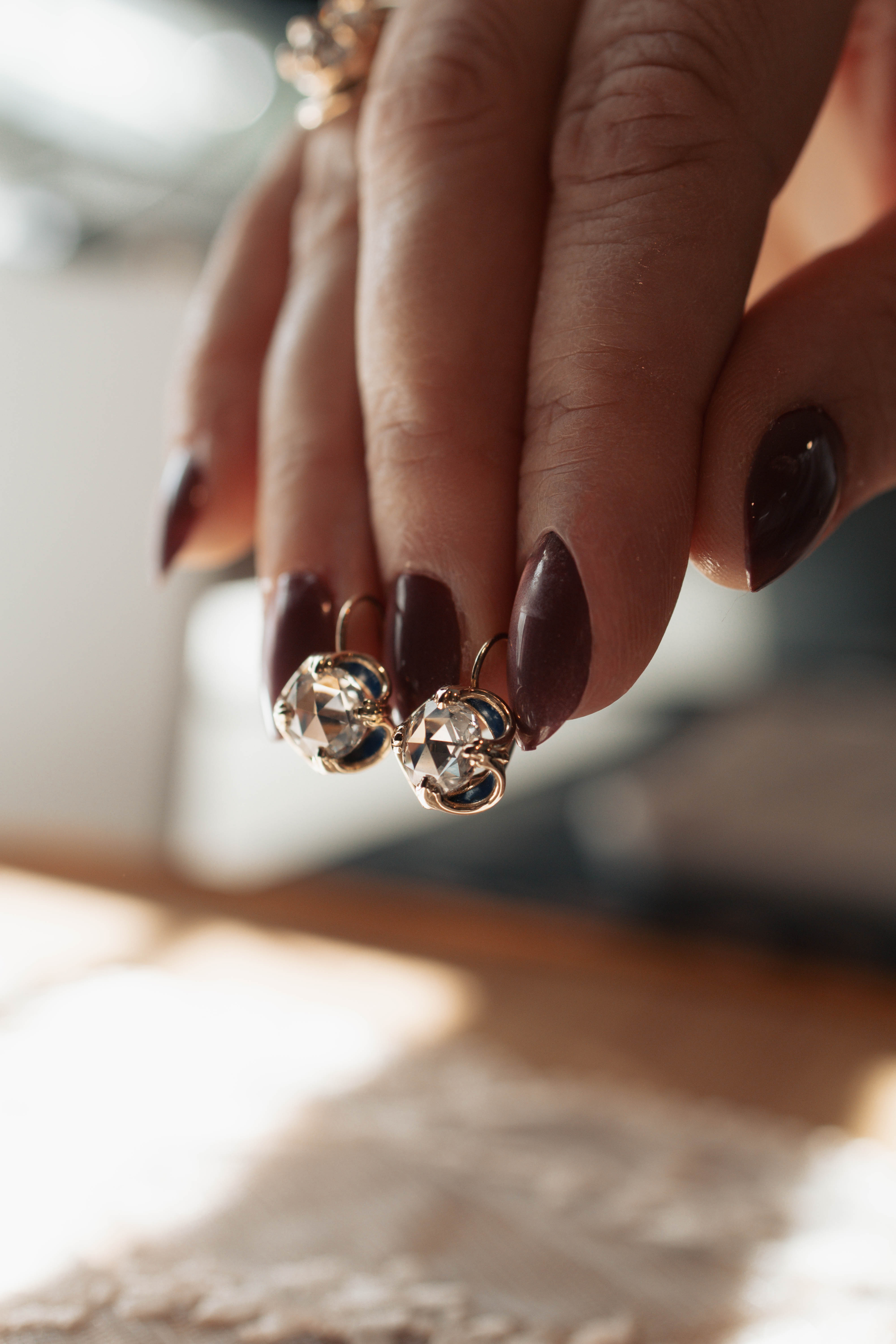 Close-up of a hand holding a pair of diamond earrings with a blurred background