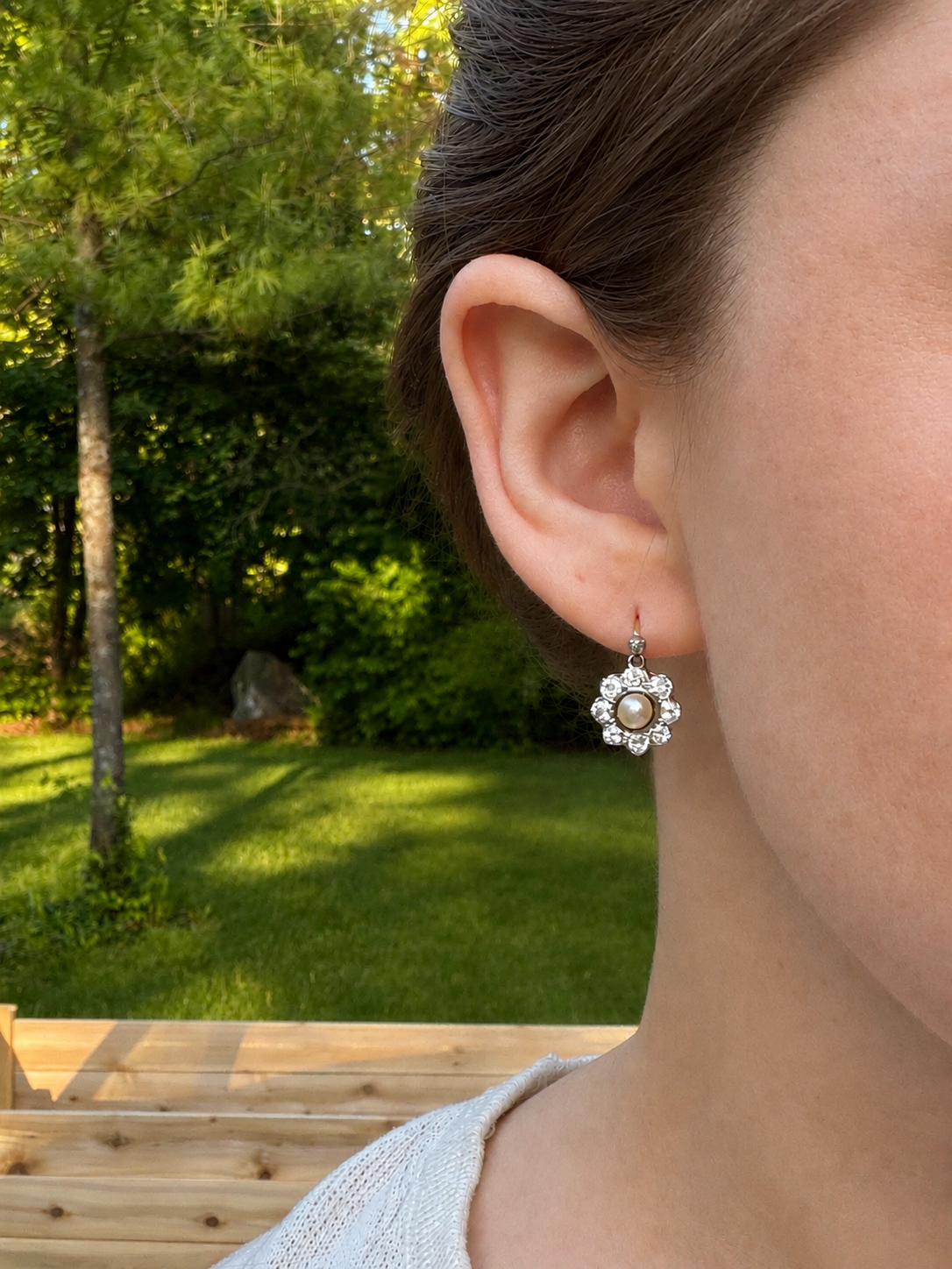 Close-up of a person wearing a floral earring of pearl and diamond with a natural outdoor background