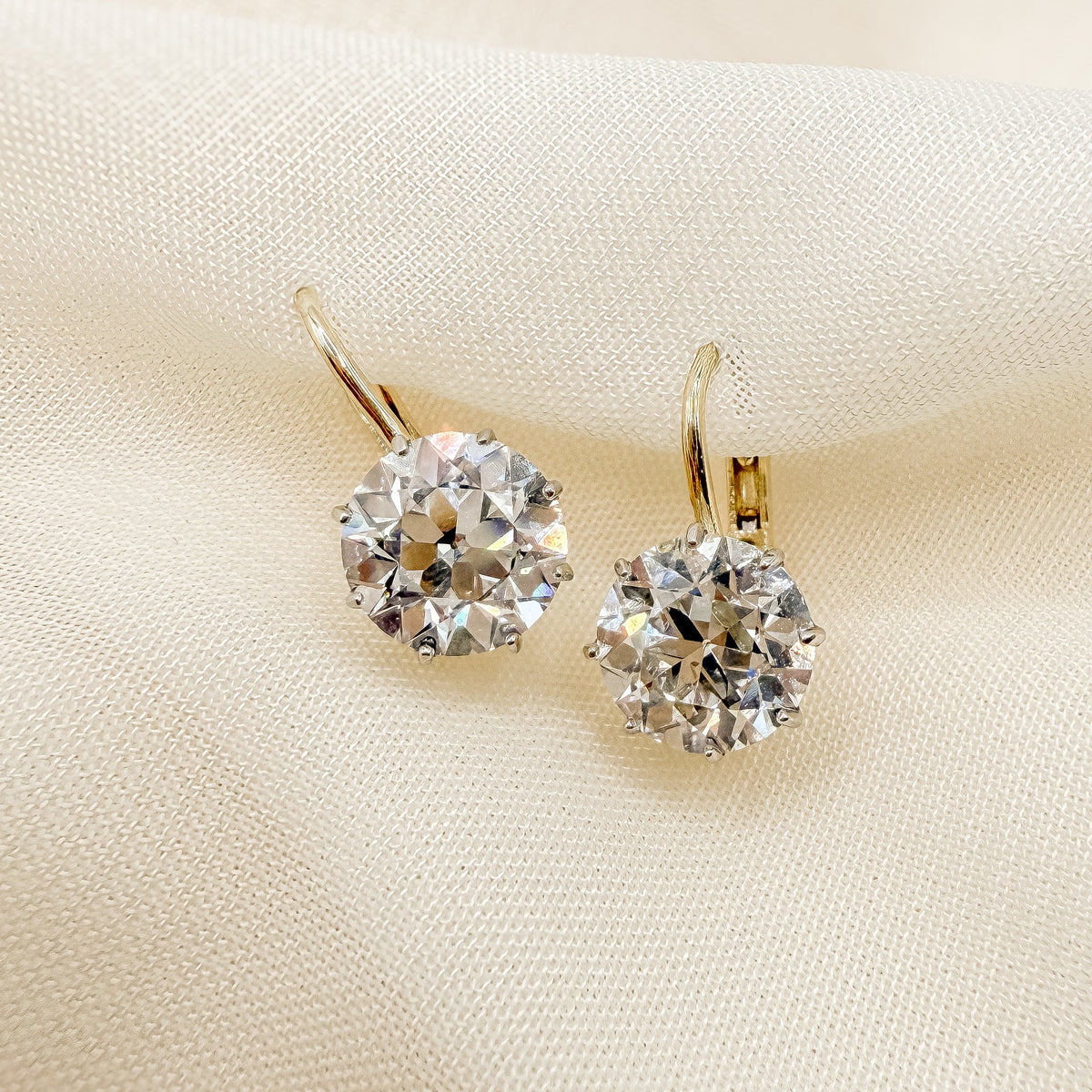A pair of gold hoop earrings with round-cut old european diamond displayed on a soft beige fabric background.