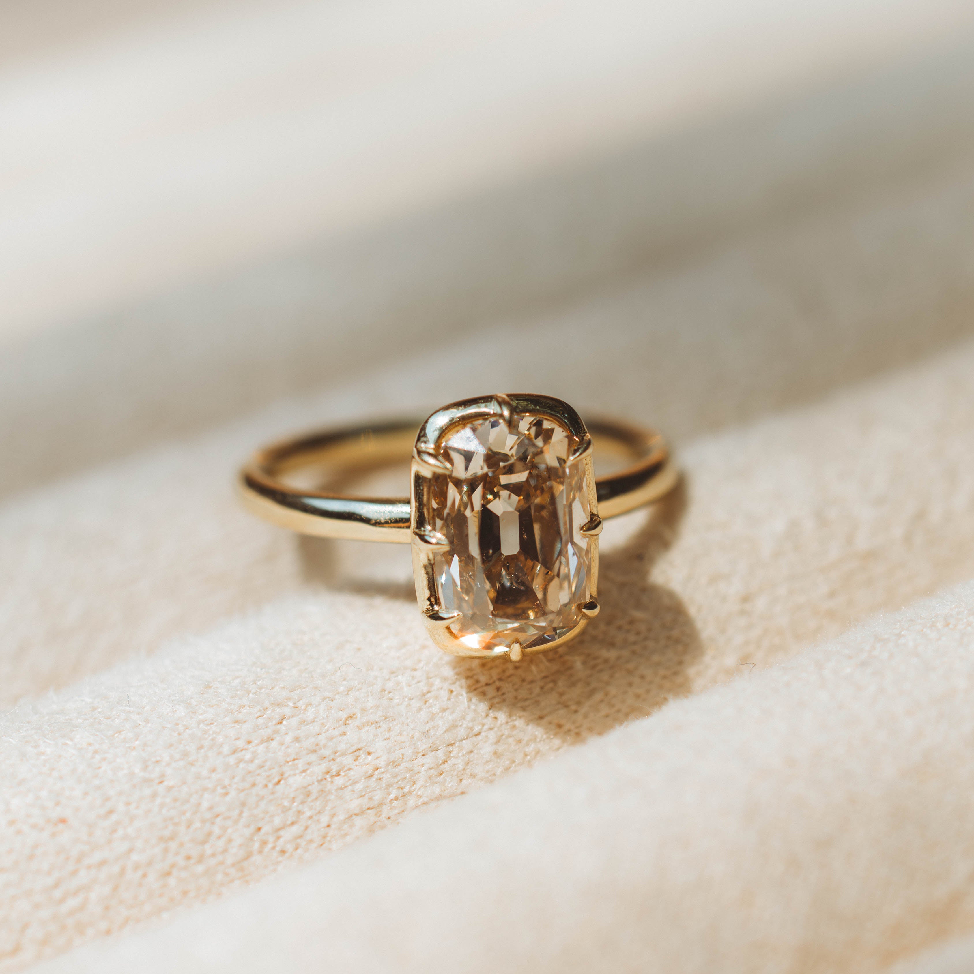 Gold ring with a large diamond on a soft beige background