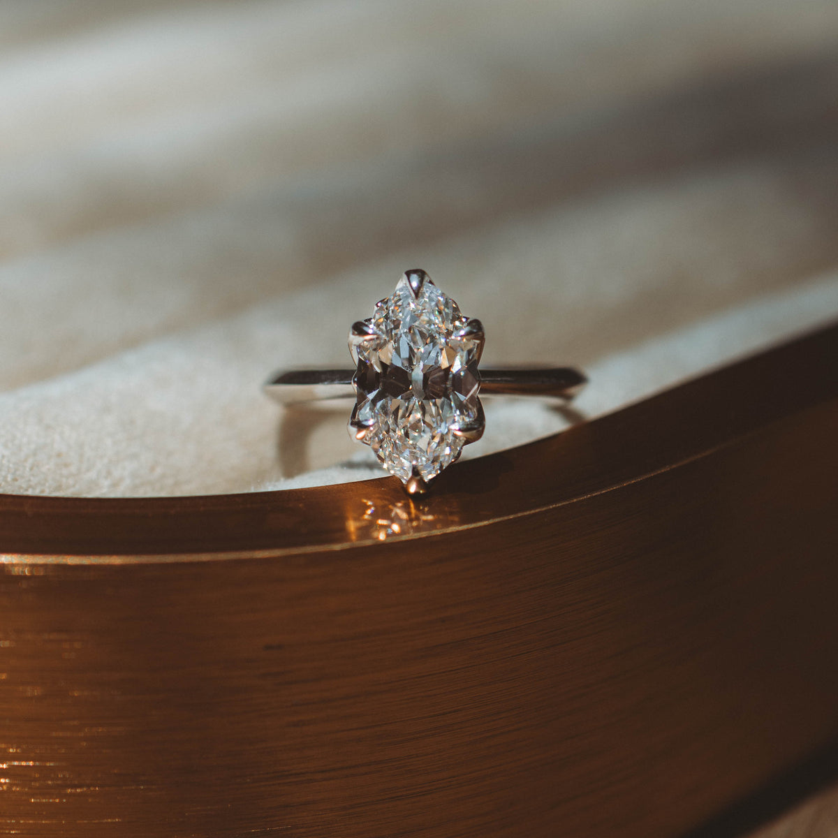 white gold moval diamond engagement ring on bronze textured surface with blurred background 