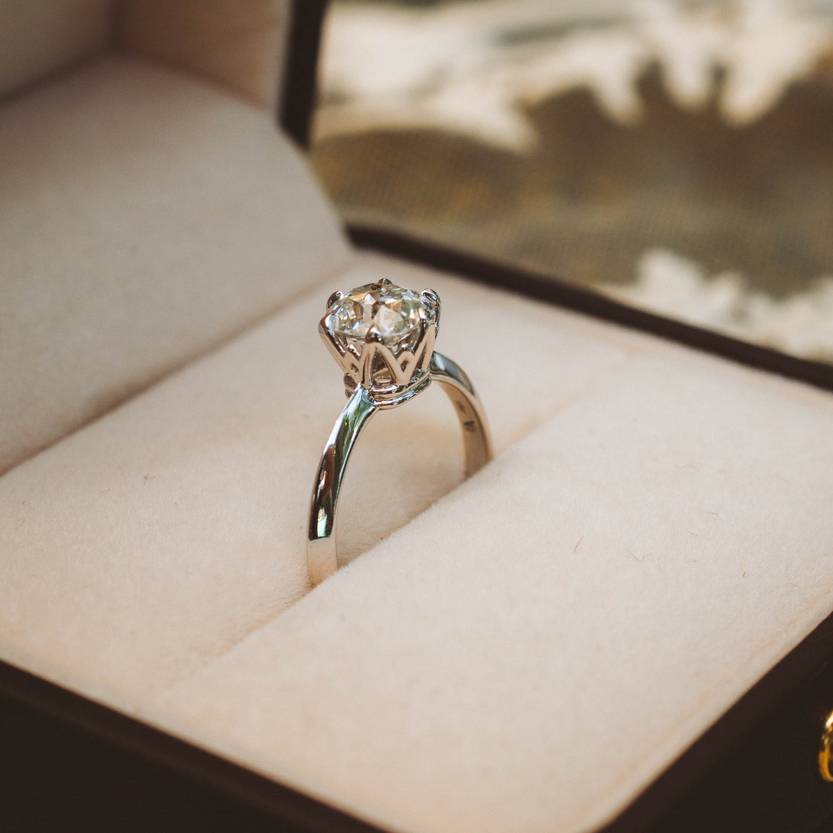 A silver engagement ring with an old mine cut natural diamond set in a cream-colored velvet ring box.