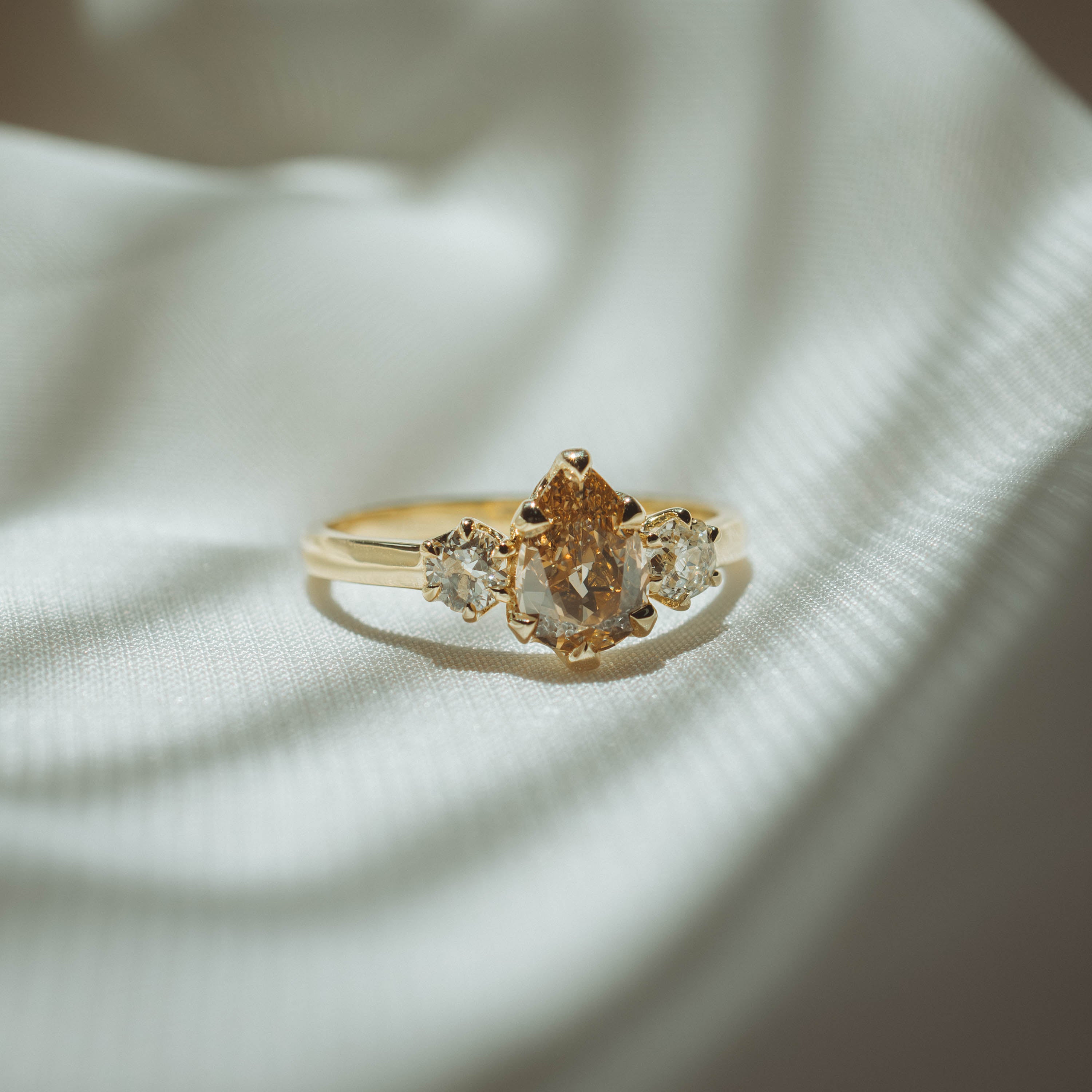 Gold ring with a central brown diamond and two smaller clear diamonds on a light fabric background