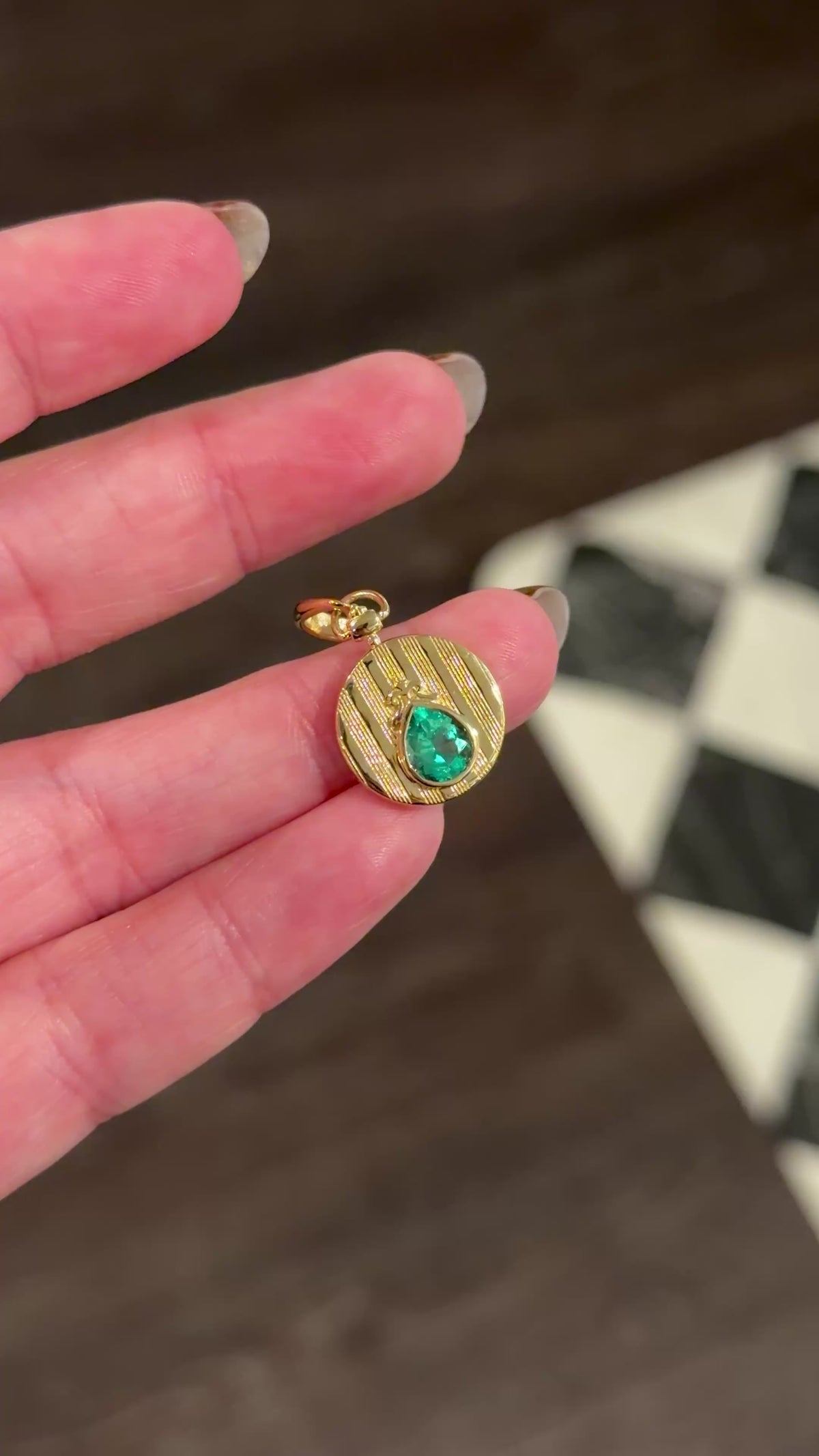 yellow gold and emerald gemstone pendant held on fingers turned back in forth in the the light