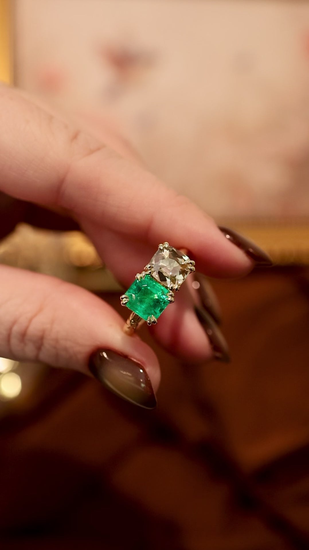 yellow gold two stone ring turned back and forth over dark background. green emerald square stone and yellow cushion diamond. 