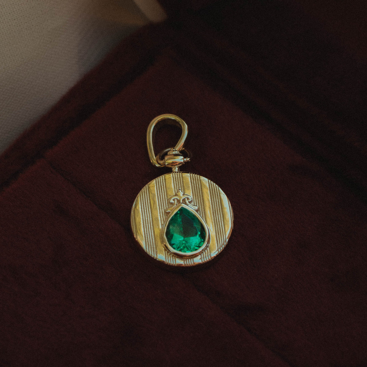 yellow gold coin pendant on velvet background featured engraved strike detail and pear shaped emerald center gemstone