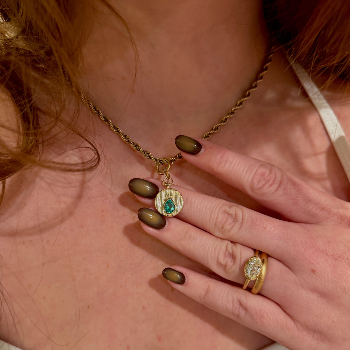 yellow gold pin stripe medallion pendant on thick yellow gold rope chain worn on model with red hair showing two gold rings on her hand held up near the medallion pendant